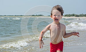 A small child runs along the seashore afraid of wave hair develop in the wind,