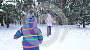 A small child runs after his mother through a snowy forest or a park on a cold winter day. Leisure, sports and games in