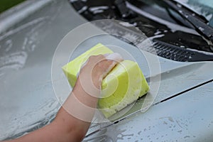 A small child`s hand with a foam sponge washes the hood of the car