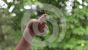 A small child`s hand pokes a finger at the window glass in the raindrops.