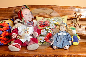 A small child in a shawl sitting on a sofa with embroidered pillows