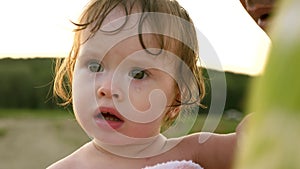 Small child sheds tears and cries while sitting in towel in hands of dad. Parent calms capricious child on beach