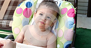 a small child sits on a baby feeding chair and eats a peach in the summer. Childhood concept. Close-up shot