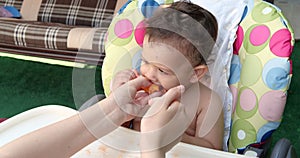 a small child sits on a baby feeding chair and eats a peach in the summer. Childhood concept. Close-up shot