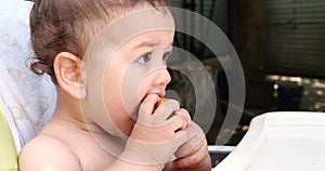 a small child sits on a baby feeding chair and eats a peach in the summer. Childhood concept. Close-up shot