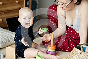 Small child sits on the floor and joyfully plays with colored toys with his mother in the interior