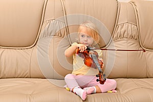 A small child sits on a leather sofa with a violin and tries to play on it
