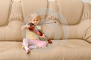 A small child sits on a leather sofa with a violin and tries to play on it