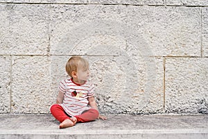 Small child sits on a stone tile against the wall and looks to the side