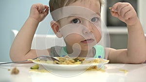 Small child is sitting at a table in a bib and eat his own spaghetti, the baby eats willingly.
