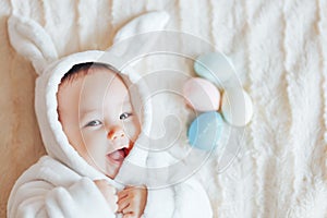 small child smiling baby in a white bunny rabbit costume easter playing with colorful easter eggs