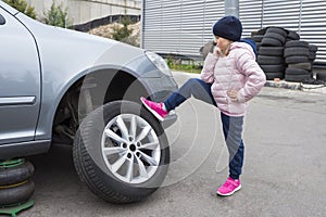 A small child standing in front of his broken car looking at the wheel