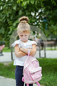 A small child stands offended on the street with a backpack. The concept of school, study, education, childhood