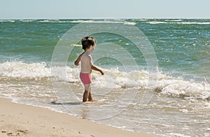 A small child stands on the seashore in the water and looks at the waves. Knows the world,