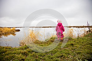 a small child stands on the shore of the lake and looks into the distance. toddler walks in nature in a winter suit