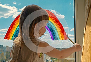 A small child stands on the windowsill and draws a rainbow on the window glass. multi-colored rainbow. symbol of happiness. select