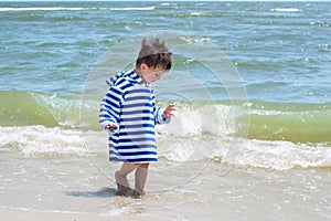 A small child in a striped robe is standing on the seashore in the water and looks at his wet legs to know the world,