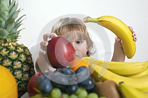 Small child takes a banana and a red apple from a fruit bowl