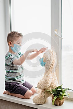 A small child with a teddy bear sits at home in quarantine in medical masks. Prevention of coronavirus and Covid - 19