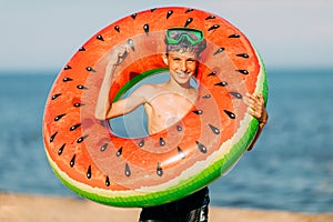 Small child teen boy in swimming glasses, with an inflatable swimming circle on the beach . Summer holiday