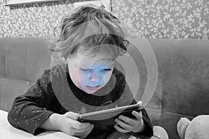 A small child of three years old sits with a phone in his hands at home. The concept of children`s addiction to gadgets, home leis