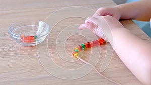 Small child, toddler stringing colored plastic beads on string, kid`s fingers close-up, concept of development of fine motor