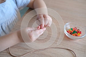 Small child, toddler stringing colored plastic beads on string, kid`s fingers close-up, concept of development of fine motor