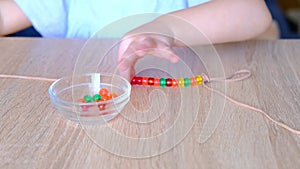 Small child, toddler stringing colored plastic beads on string, kid`s fingers close-up, concept of development of fine motor