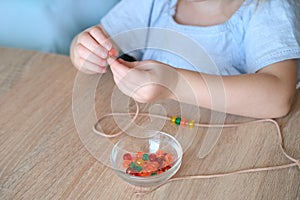 Small child, toddler stringing colored plastic beads on string, kid`s fingers close-up, concept of development of fine motor