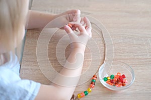 Small child, toddler stringing colored plastic beads on string, kid`s fingers close-up, concept of development of fine motor