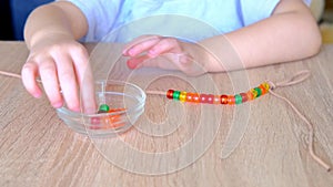 small child, toddler stringing colored plastic beads on string, kid\'s fingers close-up, concept of development of fine motor