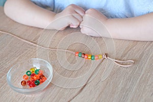 small child, toddler stringing colored plastic beads on string, kid's fingers close-up, concept of development of fine motor