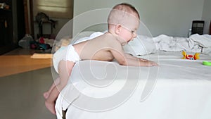 A small child is trying to get out of bed, but he does not succeed. He shakes his legs hanging them down