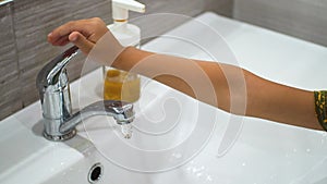 A small child turns on tap and washes his hands with soap under the running water in sink. Clean your hands to prevent