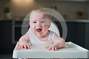 A small child in a white bodysuit sits in a high chair and smiles