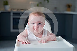 A small child in a white bodysuit sits in a high chair and smiles