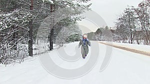 Small child in winter forest runs through snow towards camera.