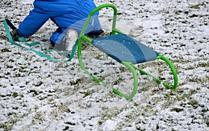 A small child in a winter jumpsuit tries to pull a sledge and still falls, crawling on his knees on the remnants of snow. holding