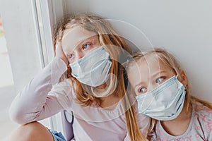 Small children in masks from coronavirus remained at home and look out the window. children are sad covid