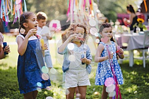 Small children outdoors in garden in summer, playing with bubbles.