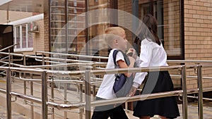 Small children are playing with backpacks in the school yard near the stairs.