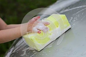 Small children`s hand with a foam sponge washes the car