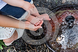 Small children's legs in mother's palms, which are lowered into a decorative garden small fountain