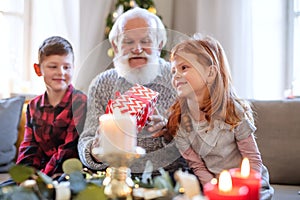 Small children with senior grandfather indoors at home at Christmas, holding presents.
