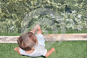 Small children sitting on the wooden pier in the water and enjoying summer day. Bare feet of boy. Vacation by the sea