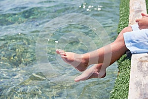 Small children sitting on the wooden pier in the water and enjoying summer day. Bare feet of boy. Vacation by the sea