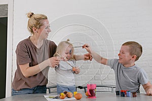 small children and their mother play with paints paint each other at home in the kitchen while preparing for the Easter