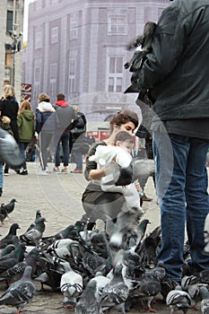 Small children on a winter day playing in a square in a European city. They enjoy chasing pigeons and feeding them