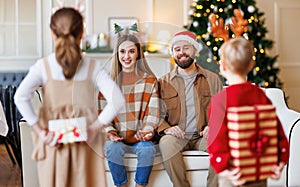 Small children with wrapped gift boxes behind back making surprise for parents on Christmas morning