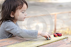 a small children& x27;s hand points to one toy car among a multitude of cars on a wooden red-yellow table